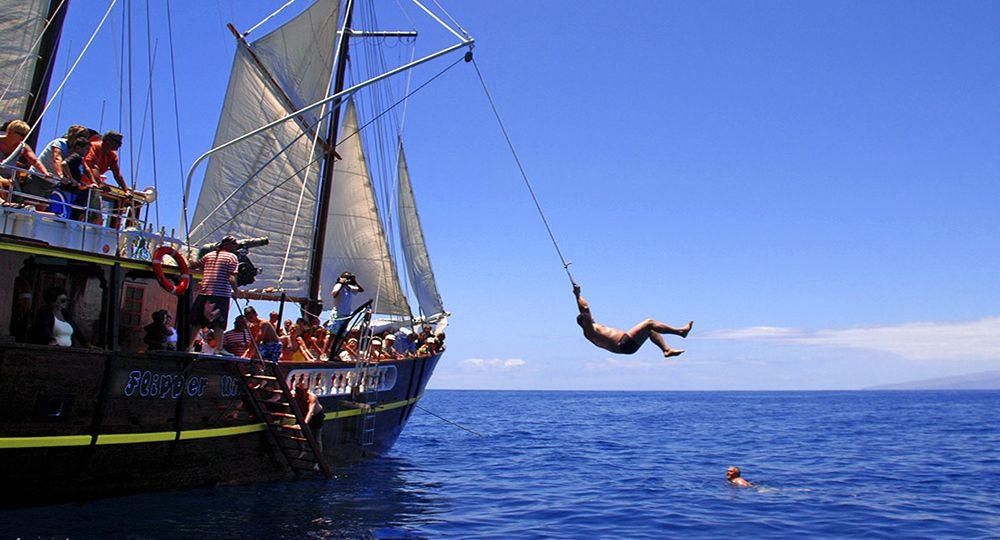 Un hombre colgado del lado de un barco en el agua.