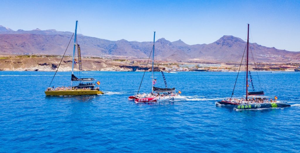Tres barcos en el océano con montañas al fondo, creando un paisaje sereno y natural.