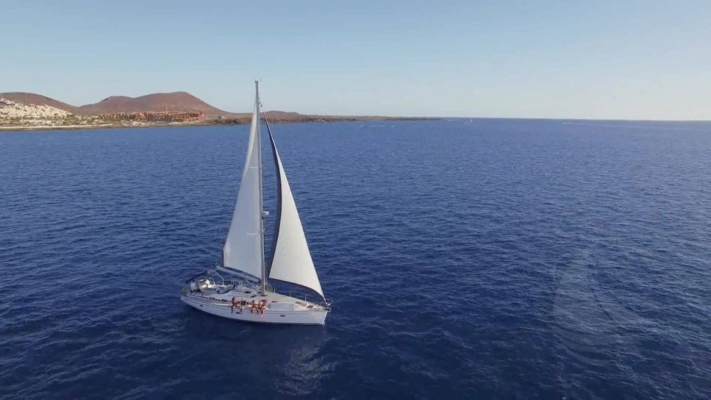 Un velero navega en el océano abierto con montañas al fondo.