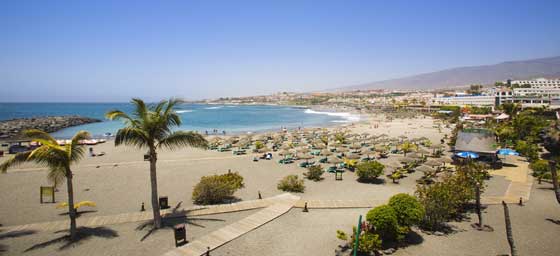 Playa en Tenerife, España, con arena dorada y aguas cristalinas bajo un cielo despejado.